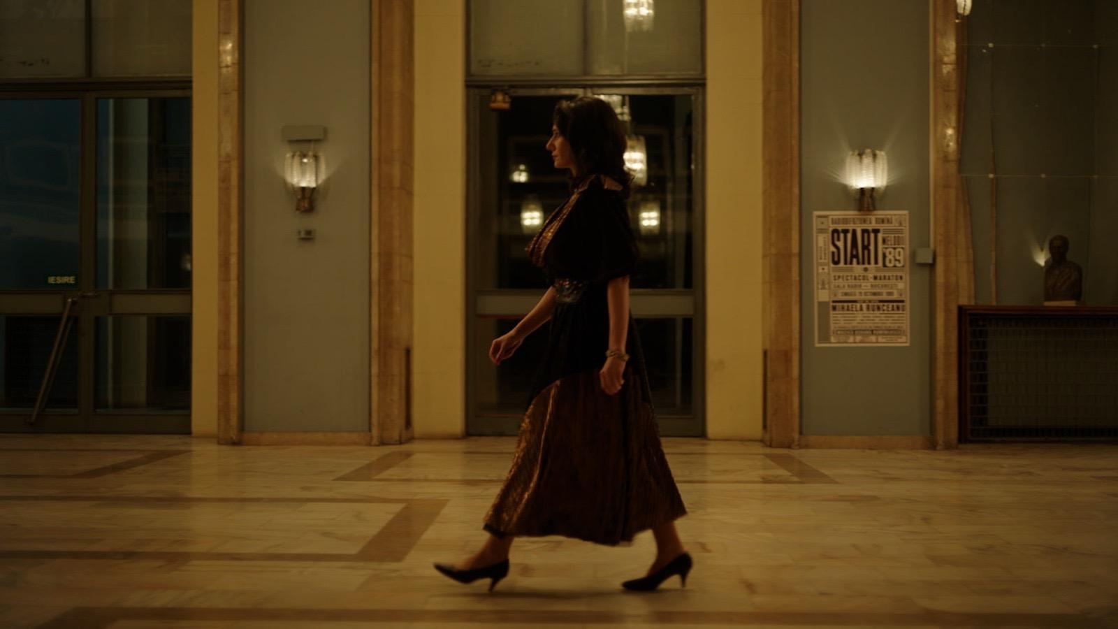 Film still: a woman in burgundy dancing in a large room
